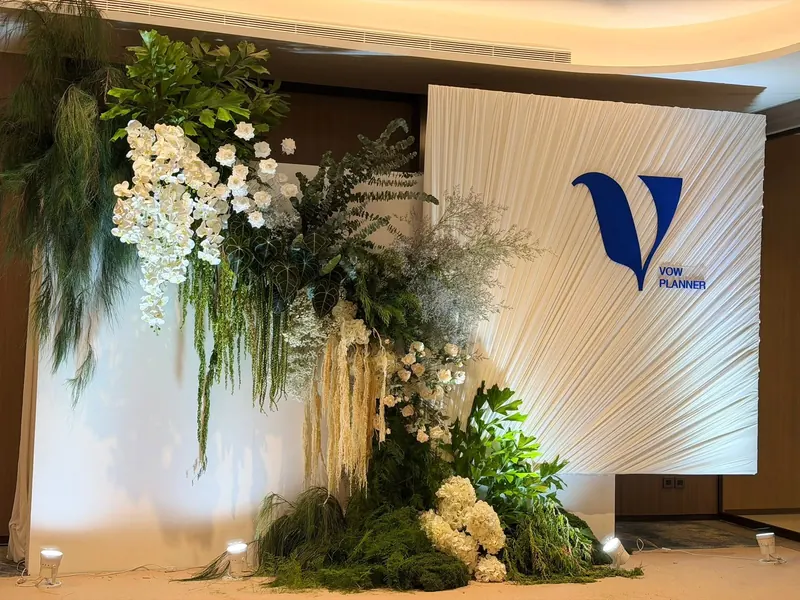 ผนังผ้าจีบรัศมี กับโลโก้ V ของ Vow Planner และดอกไม้ขาวเขียว